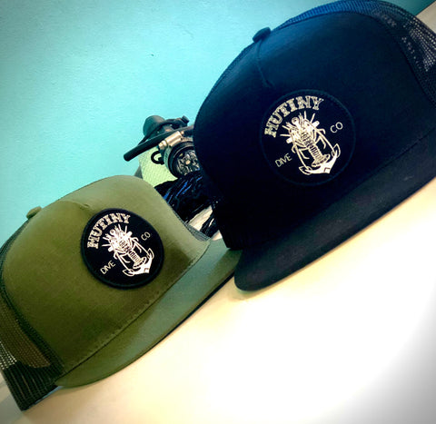 two Mutiny Dive Co hats. one in green and one in black.