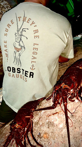 Josh wearing the Mutiny Lobster Gauge Tee, in tan, standing in front of a couple lobsters that were hauled in.